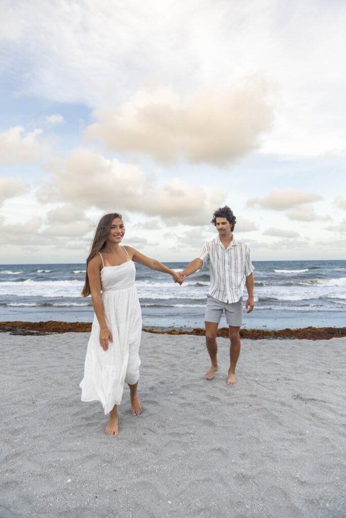 Engaged couple walking hand in hand on beach West Palm Beach engagement photographer romantic stroll