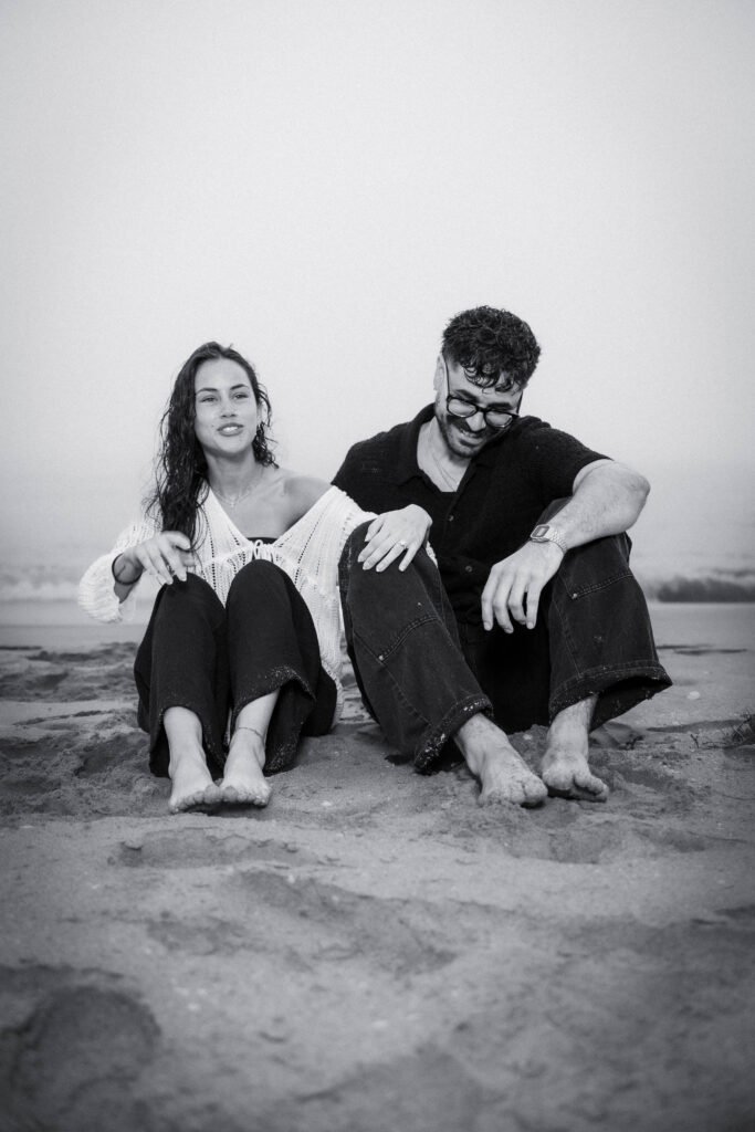 Black and white artistic couple sitting on beach West Palm Beach engagement photographer moody