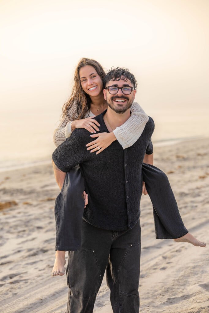 Happy engaged couple piggyback hug on beach West Palm Beach engagement photographer joyful