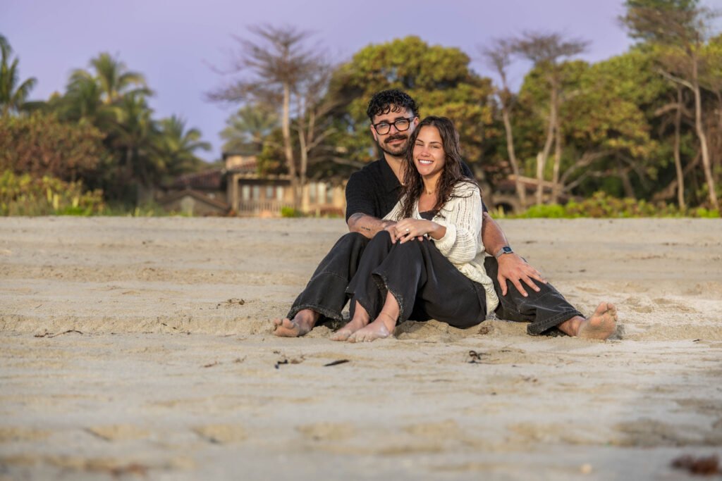 Couple sitting beach sand with palm trees background West Palm Beach engagement photography