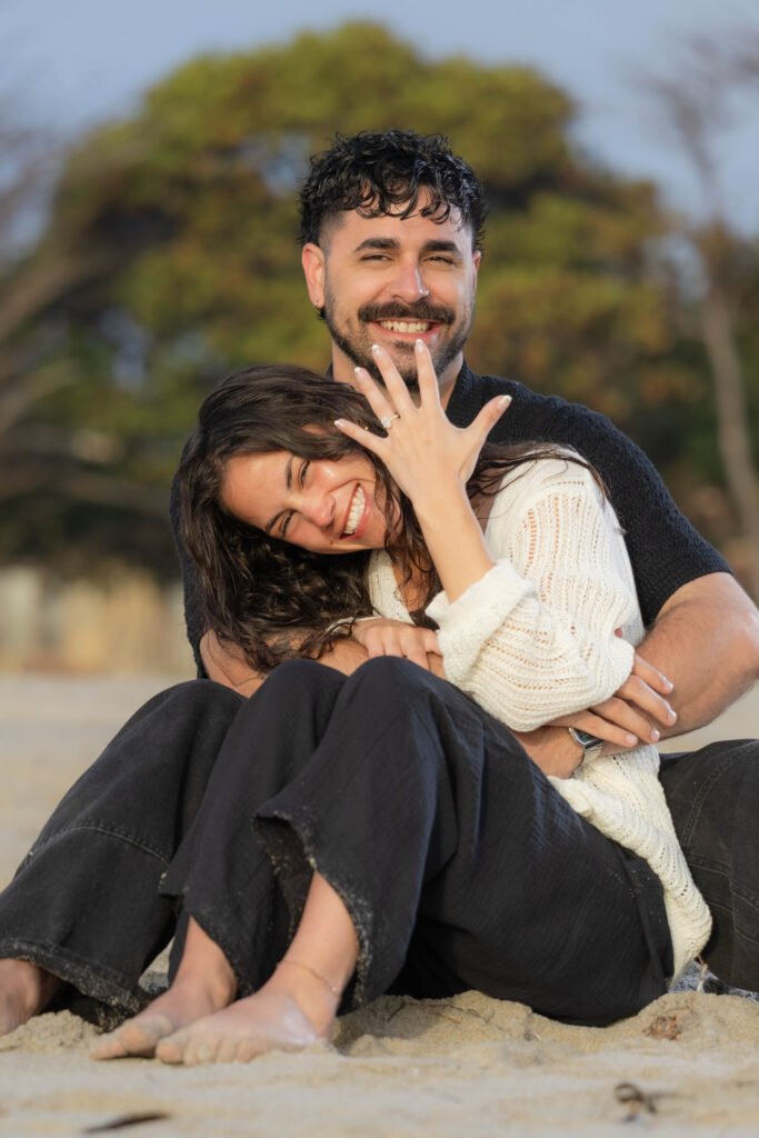 Engaged couple showing ring sitting on beach West Palm Beach engagement photographer joyful portrait