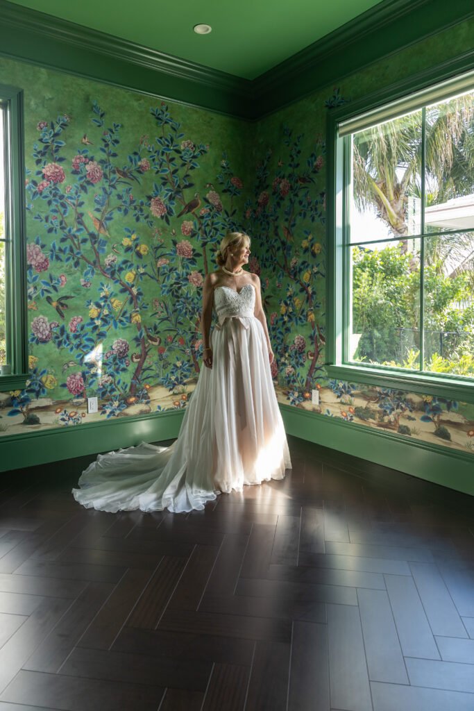 Bride in an elegant wedding dress posing in a green floral wallpaper room, West Palm Beach bridal photography by The Love Pics
