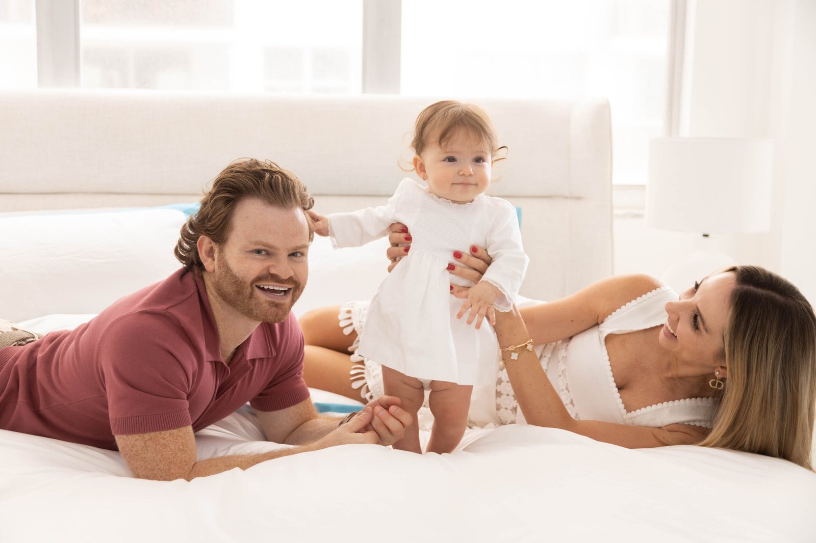 Family portrait with smiling parents and their baby girl in a white dress at an indoor studio session