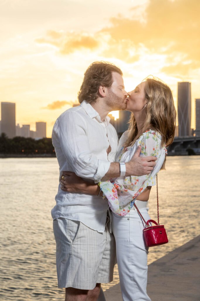 Close-up portrait of a couple kissing at sunset with Miami skyline and water background during an engagement session