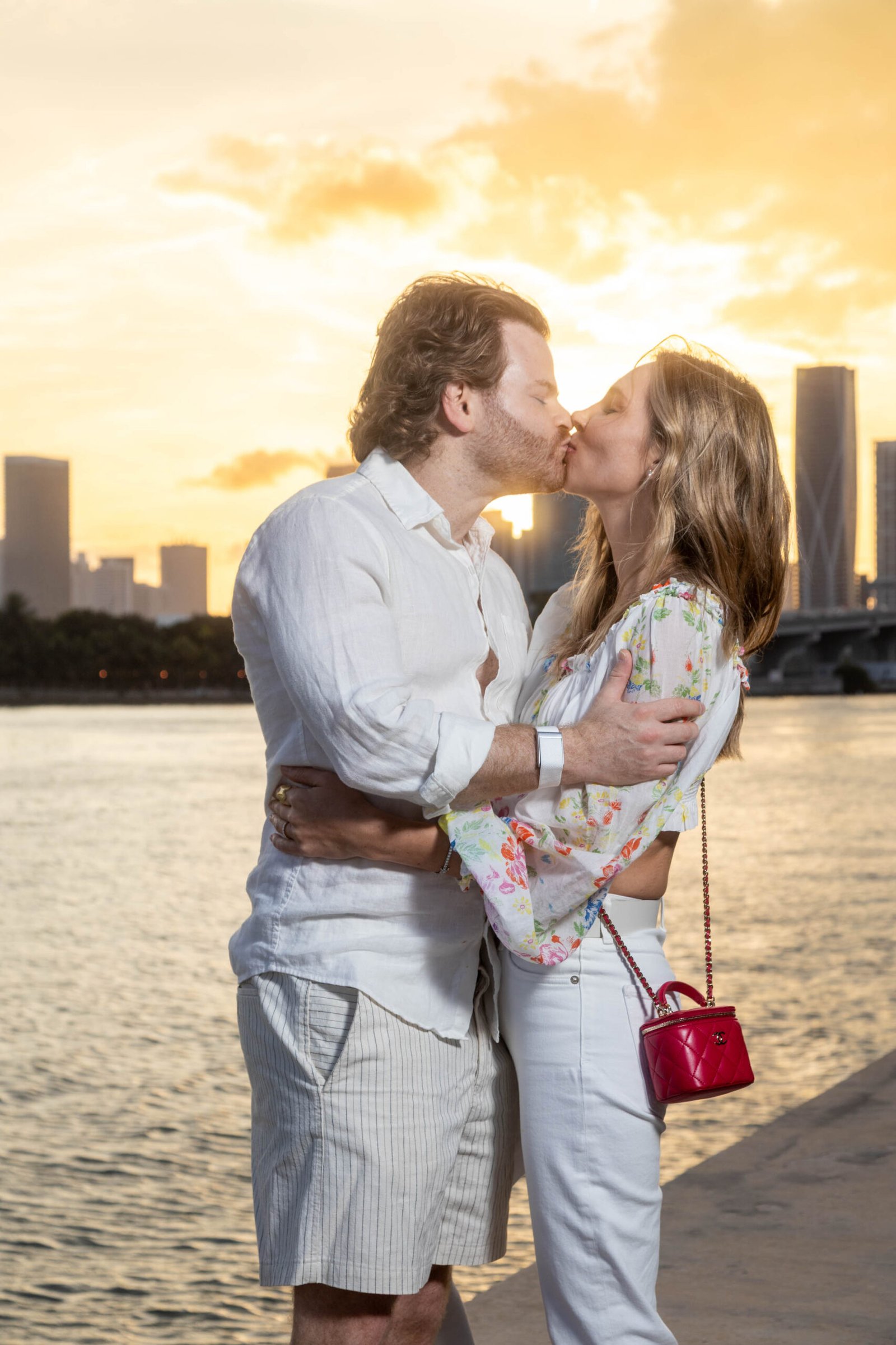 Couple kissing at sunset with the Miami skyline behind them during an engagement session