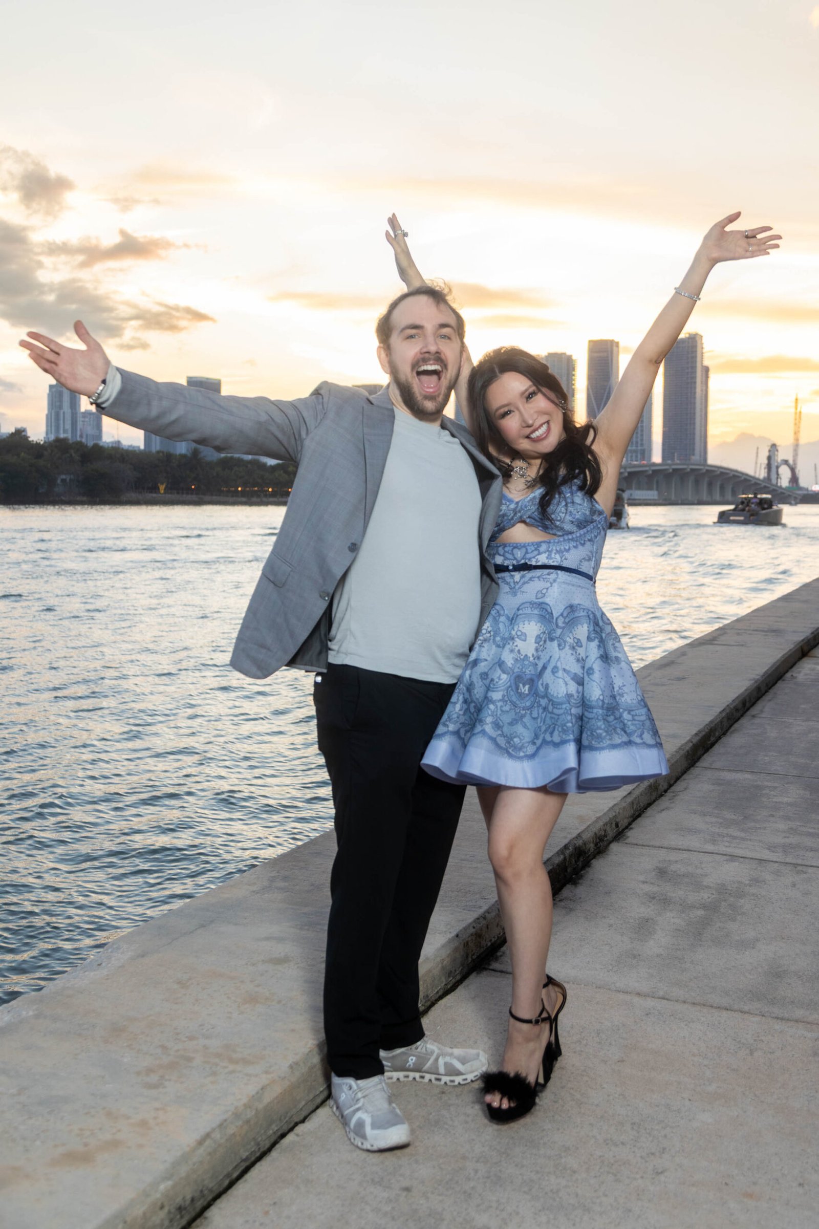 Young couple posing at sunset by the Miami skyline during an engagement session