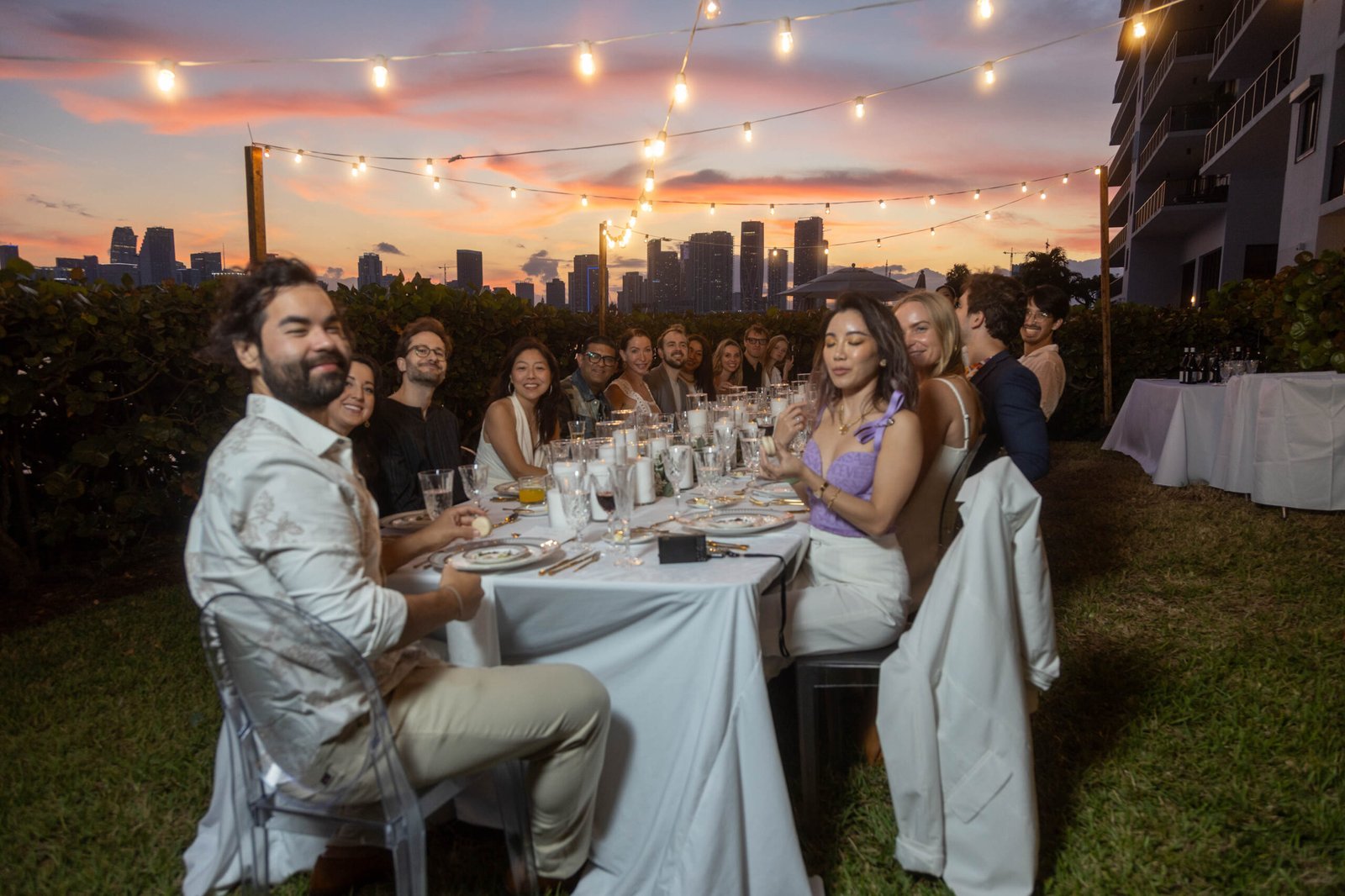 Guests dining at a long table under string lights at dusk in Miami