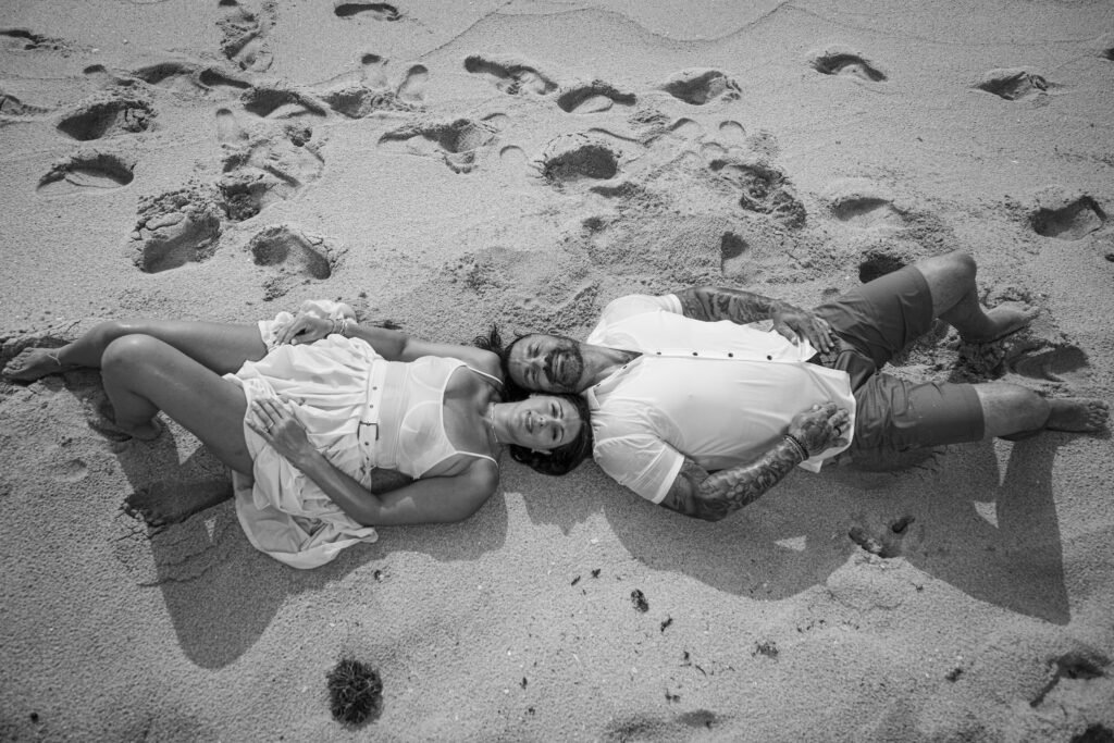 Engaged couple lying on sand with footprints aerial view black and white West Palm Beach engagement photography