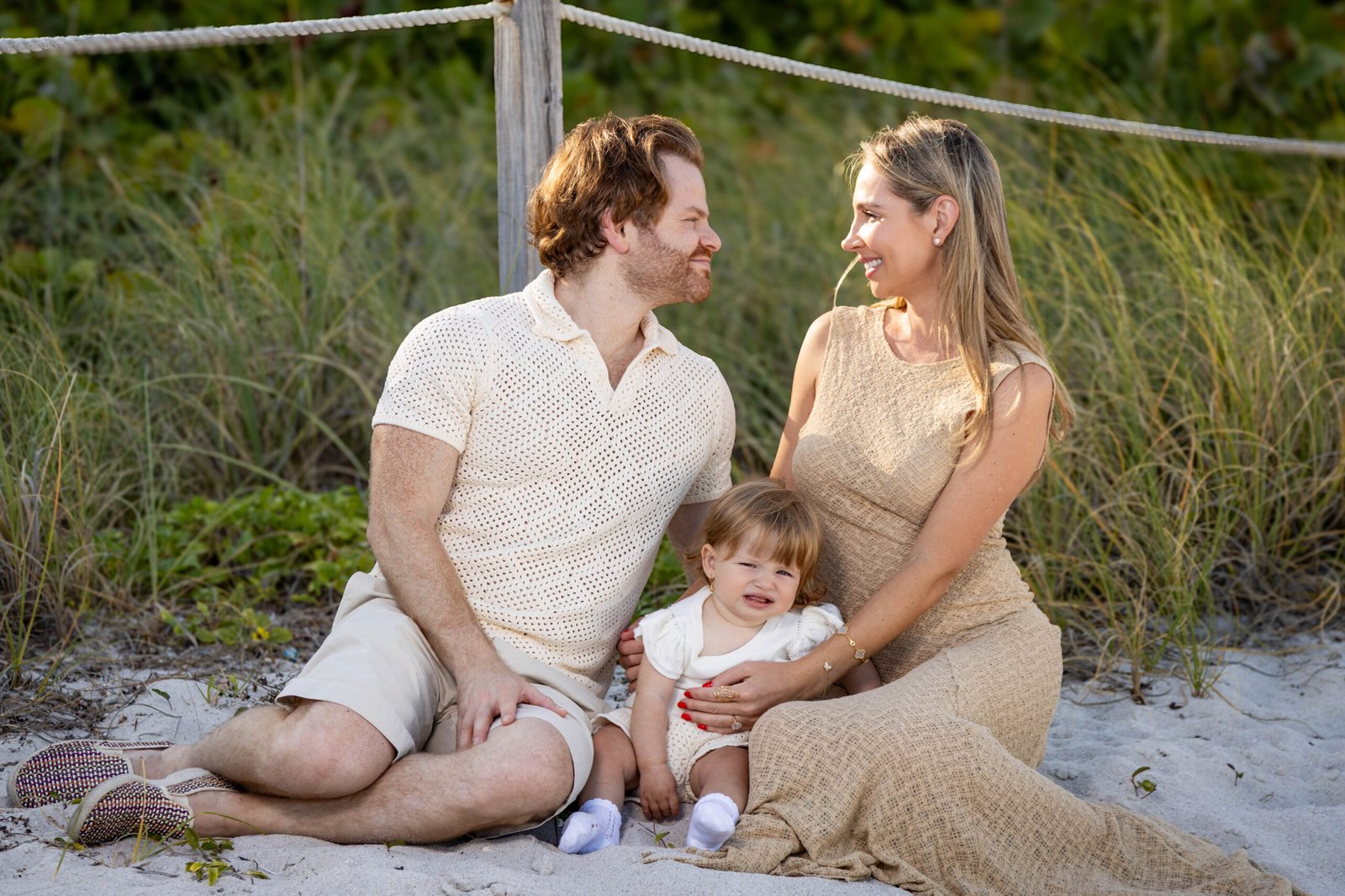 Expectant family kneeling together on the sand during a maternity beach session in South Florida