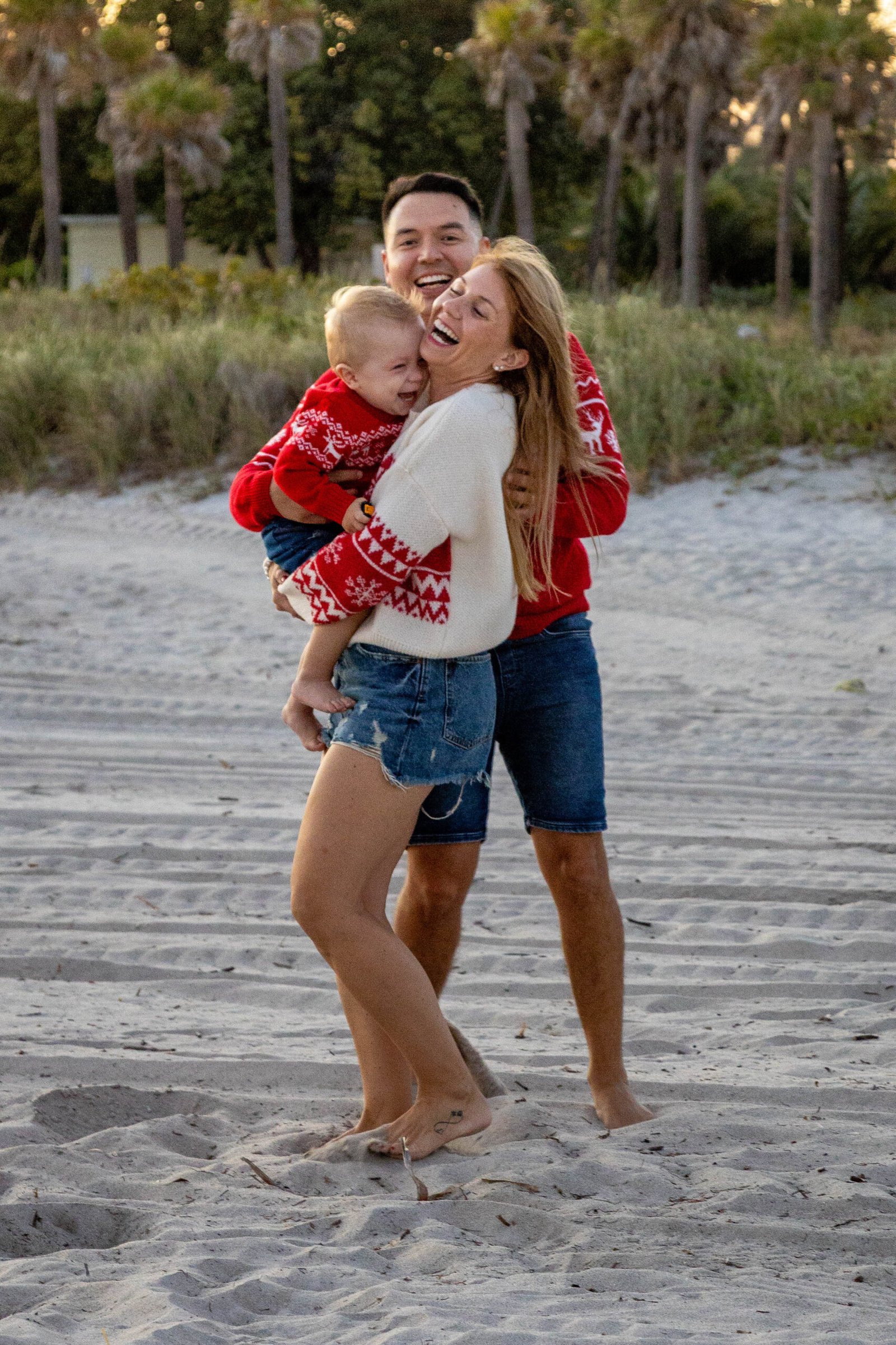 Family in matching red holiday sweaters lifting their child on the beach in West Palm Beach
