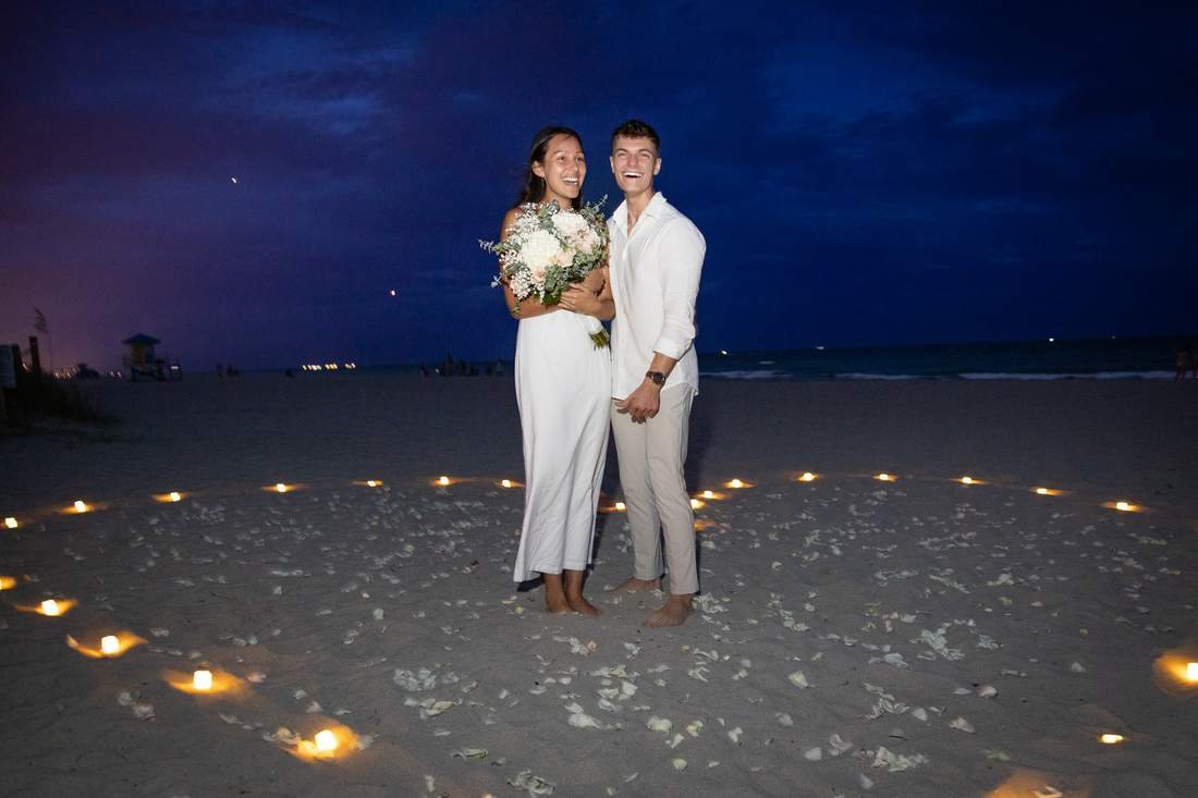 Just-engaged couple posing inside a heart of candles during their West Palm Beach beach engagement session at dusk