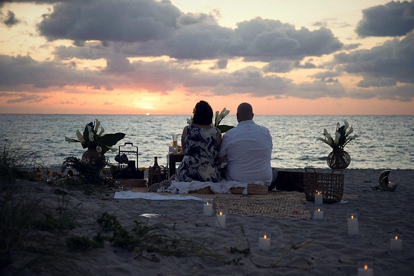 Couple at a candlelit boho beach picnic setup watching the sunrise over the ocean at Las Olas Beach, Fort Lauderdale