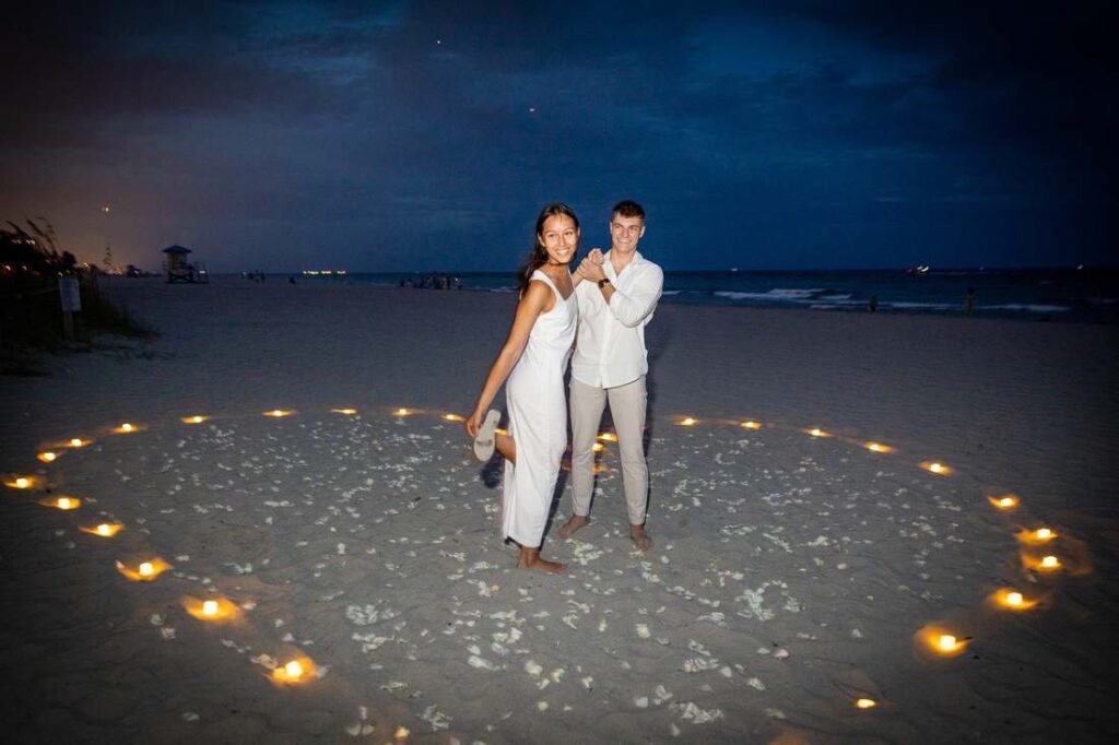 Engaged couple standing inside a glowing candle heart on the sand at dusk during a West Palm Beach beach engagement session