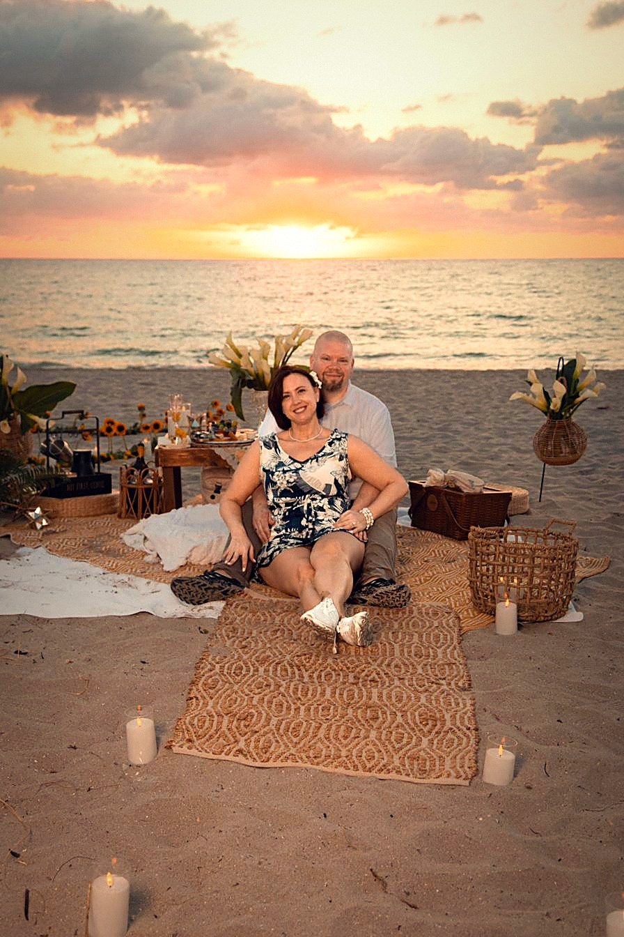 Couple at a luxury boho beach picnic proposal setup with sunflowers and candles at sunrise, Fort Lauderdale