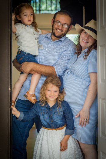 Father and mother with their two young daughters smiling in their doorway family portrait