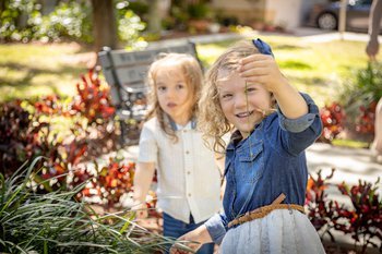 Two young sisters playing happily in a sunny garden surrounded by red flowers