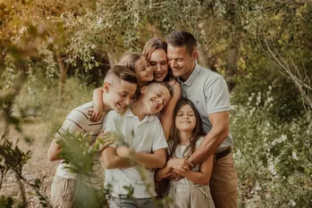 Large family group with parents and four children of different ages embracing in a park
