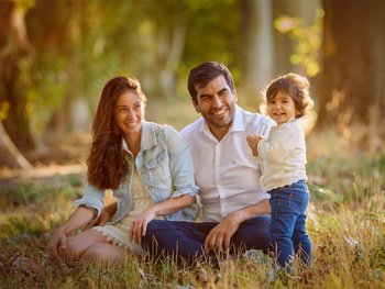 Young couple with their toddler son sitting in a tall grass field at golden hour