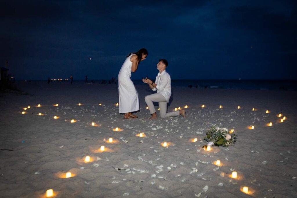 Surprise marriage proposal on one knee surrounded by candles and rose petals on a West Palm Beach beach at twilight