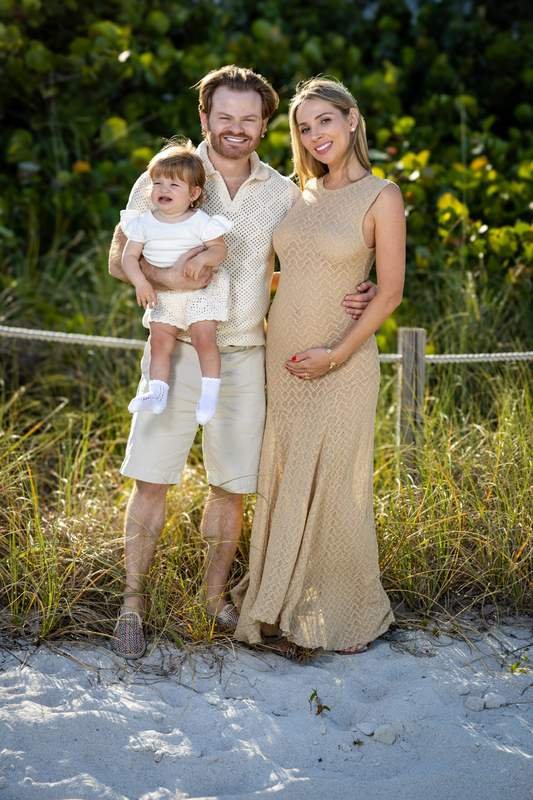 Retrato familiar de cuerpo entero con su hija pequeña en la playa al atardecer