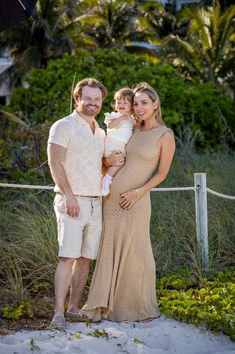 Padres e hija pequeña sonriendo en la playa durante una sesión familiar al atardecer