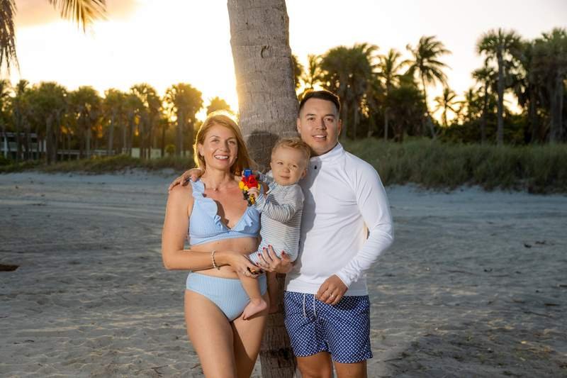 Familia joven posando junto a una palmera en la playa al atardecer