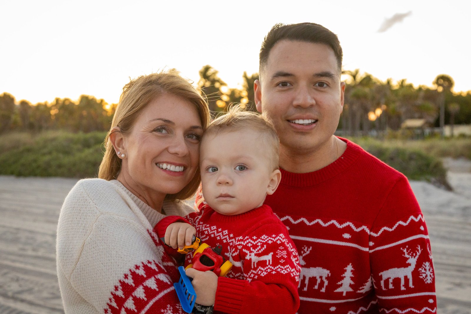 Family portrait at the beach during sunset with parents and son in red Christmas sweaters