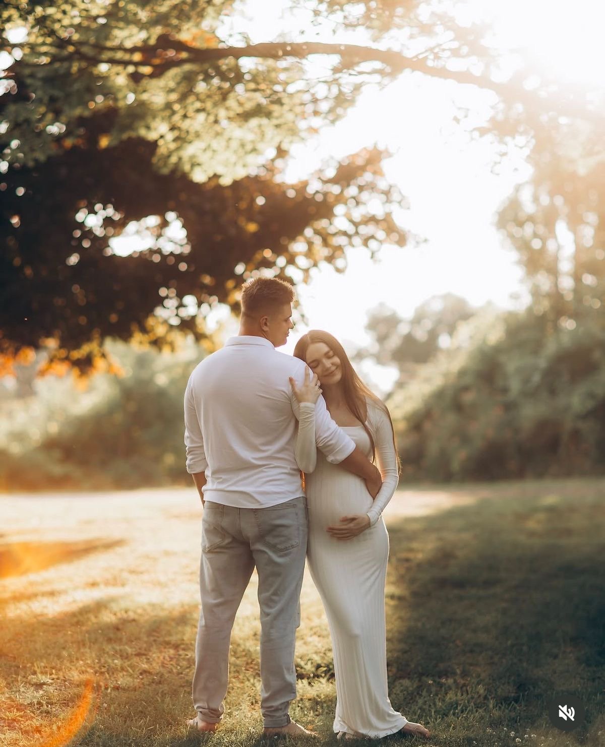Expecting couple holding the bump together in a field at golden hour