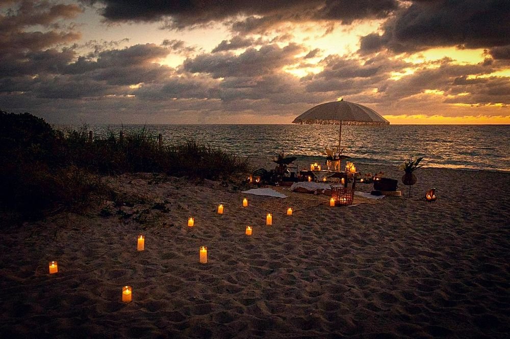 Montaje de propuesta en la playa con velas y flores al amanecer