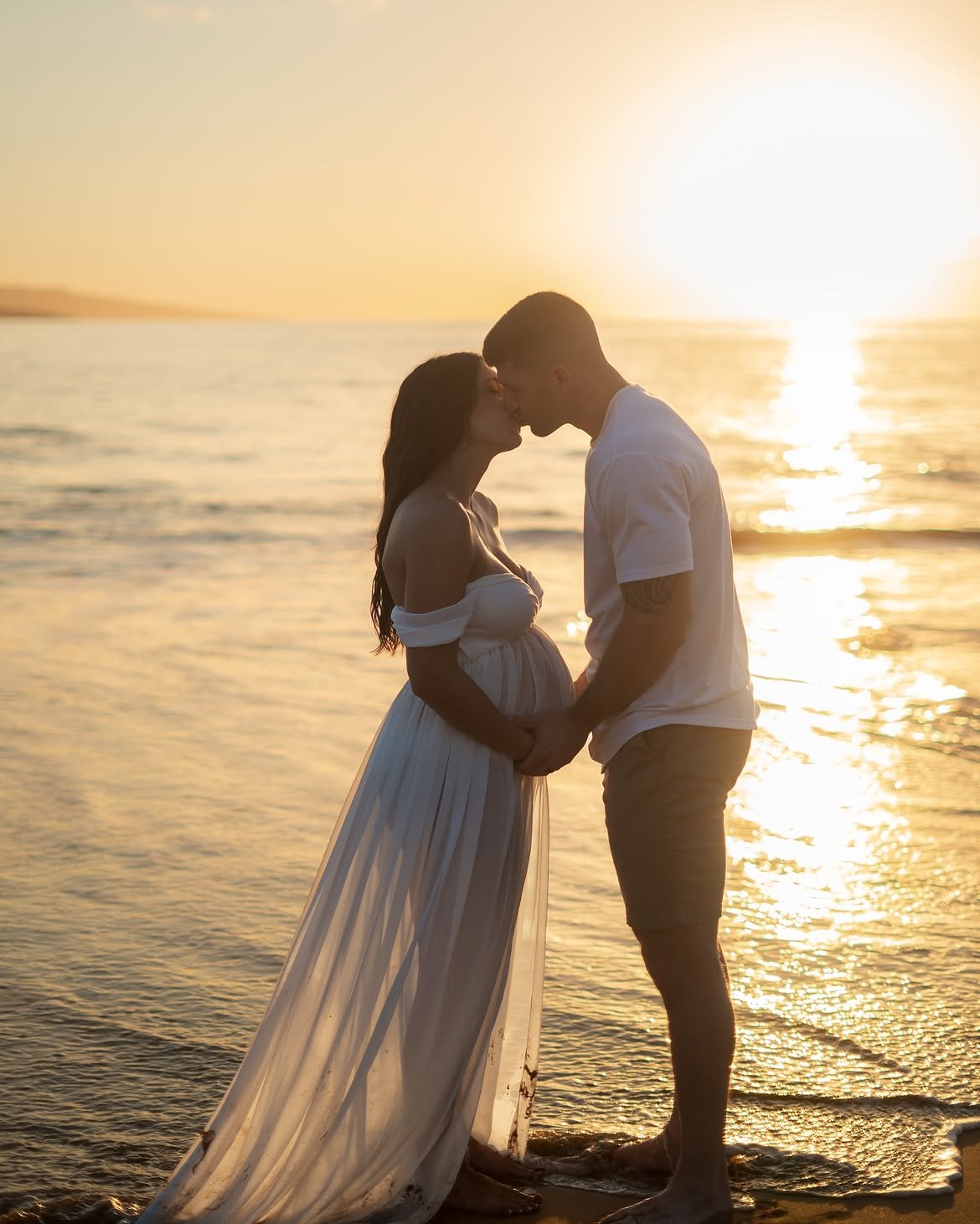 Couple embracing during a sunset maternity photo session on the beach