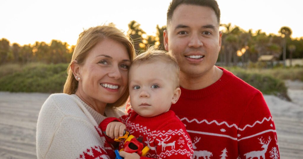 Family portrait at the beach during sunset with parents and son in red Christmas sweaters