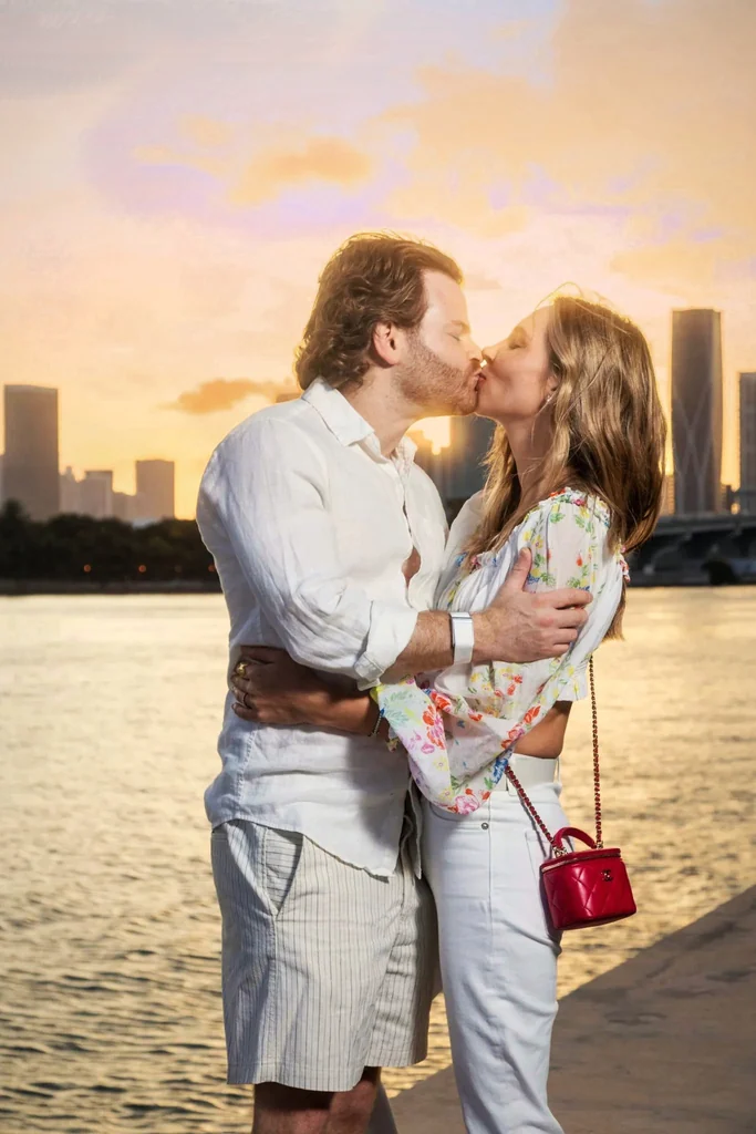 Close-up portrait of a couple kissing at sunset with Miami skyline and water background during an engagement session