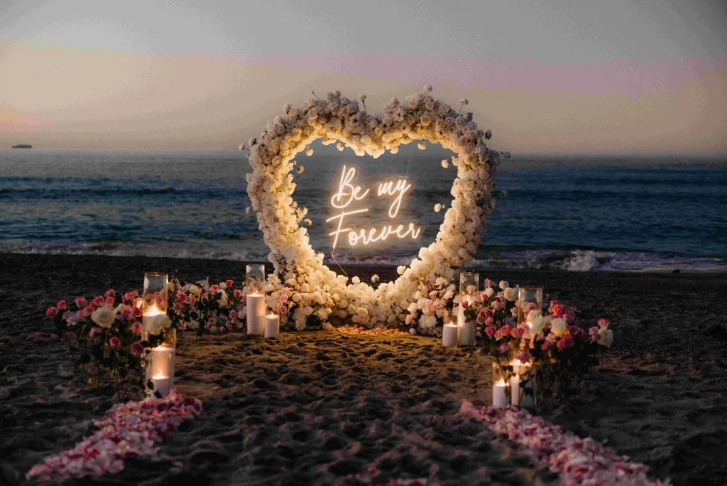 Luxury heart-shaped floral arch with Be My Forever neon sign and candles on the beach at sunset — West Palm Beach proposal setup by The Love Pics