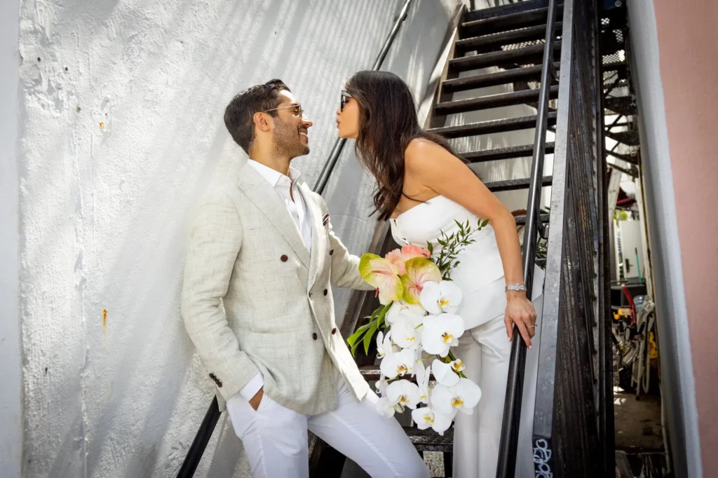 Bride with orchid bouquet smiles at the groom on an outdoor staircase in Miami Beach