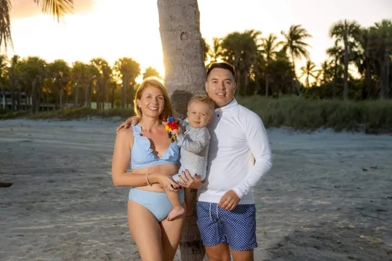 Familia joven posando junto a una palmera en la playa al atardecer