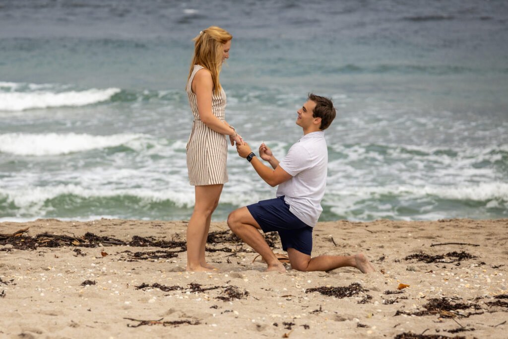 Man on one knee proposing on the beach in Palm Beach Shores, Singer Island, under a cloudy sky